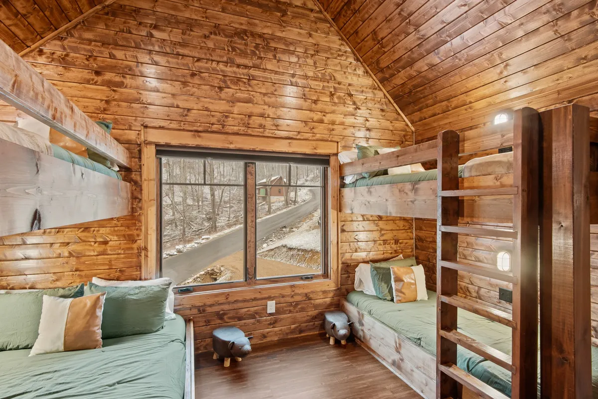 A playful and inviting bunk room with multiple wooden bunk beds, a large window, and wooden walls. The space is designed for group fun and sleepovers, fostering connection and lightheartedness.