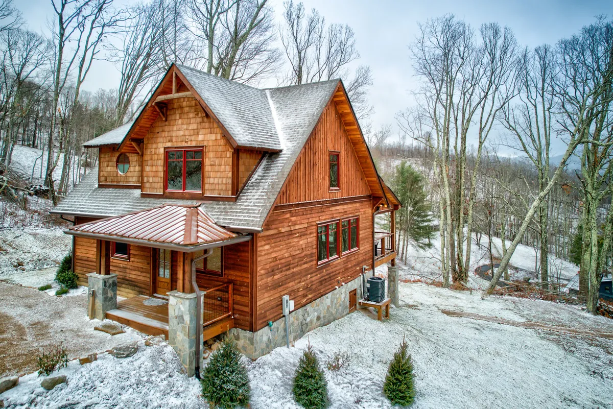 A welcoming view of the wooden exterior of a cabin at Eagles Nest, framed by sloped roofs and expansive windows, all nestled among tall trees. The setting is tranquil, evoking a sense of natural adventure and relaxation, with hints of nearby trails and outdoor activity possibilities.