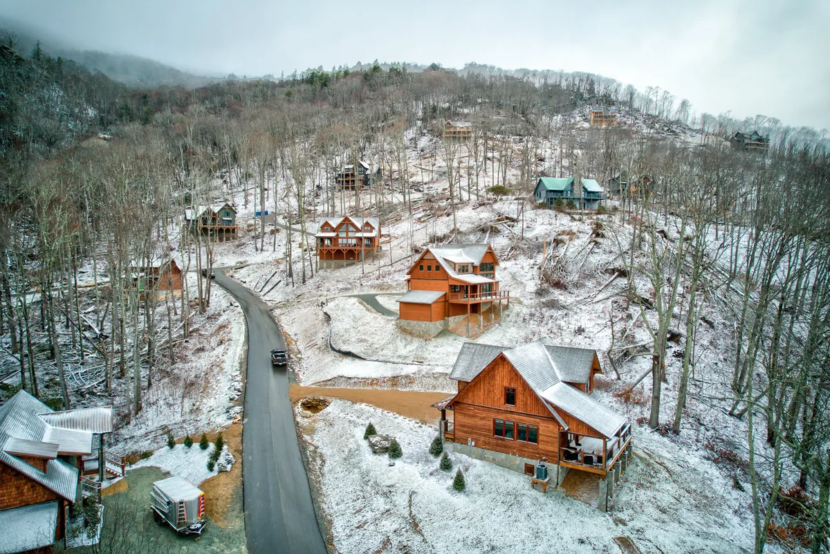 Multiple wooden cabins dot a snow-covered landscape, bordered by a winding road and tall trees. The scene captures the communal spirit and vastness of the resort, suggesting access to a range of amenities and activities within the Eagles Nest community.