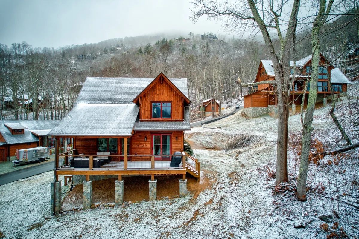 A peaceful scene outside a wooden cabin with porch seating and a snow-covered landscape. The inviting porch suggests a space to relax after outdoor adventures, while the open grounds hint at the possibility of nature walks and group activities.