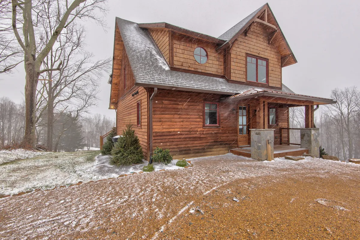 A welcoming wooden cabin with dormer windows and a front porch, framed by a snowy yard. The inviting porch and visible yard space suggest ample opportunities for outdoor family gatherings, games, and relaxation after a day of adventure.