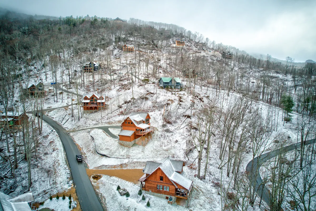 Multiple wooden cabins dot a snow-covered landscape, with a winding road leading through the serene scene. The area is surrounded by trees, inviting families to imagine hiking, playing in the snow, or enjoying group activities just outside their doorstep.