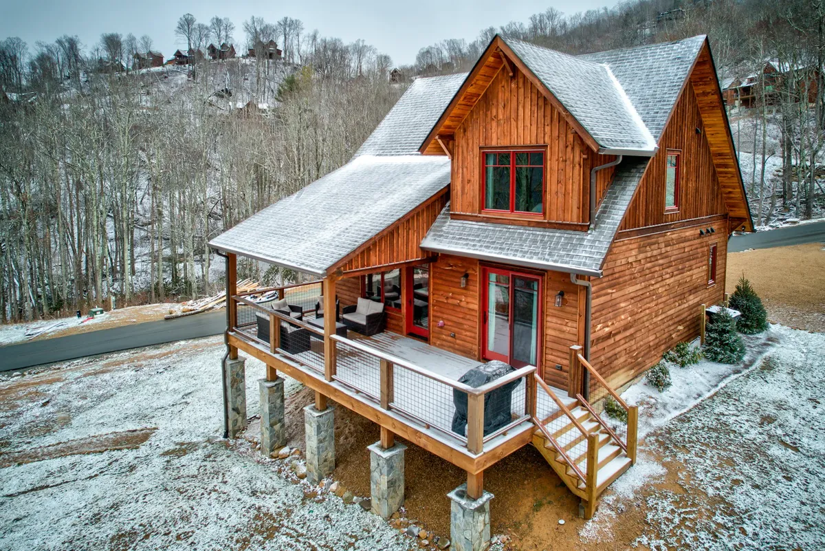 A cozy wooden cabin with a snow-covered roof and an inviting deck area. The outdoor deck provides a gathering space to enjoy the landscape or unwind after a day of adventure, tying into both relaxation and activity.